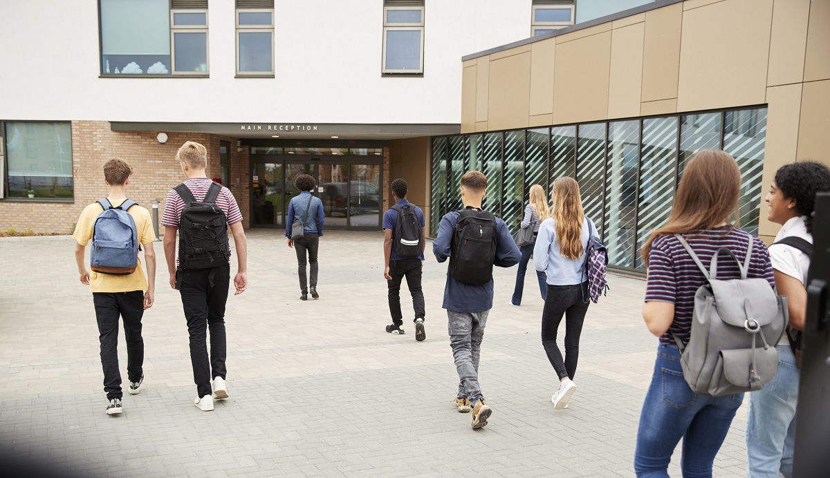Rear view of high school students walking into a building