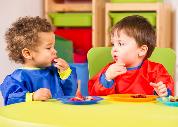 Two toddlers eating fruit in a nursery