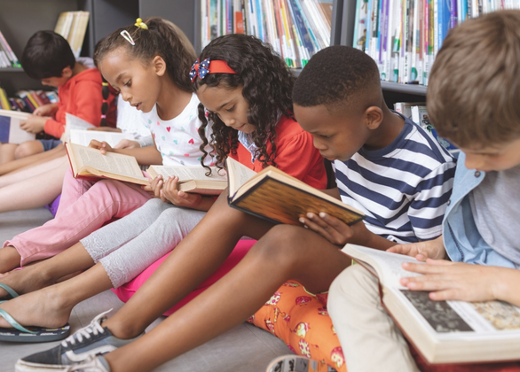 School kids sitting on cushions and studying over books in a library
