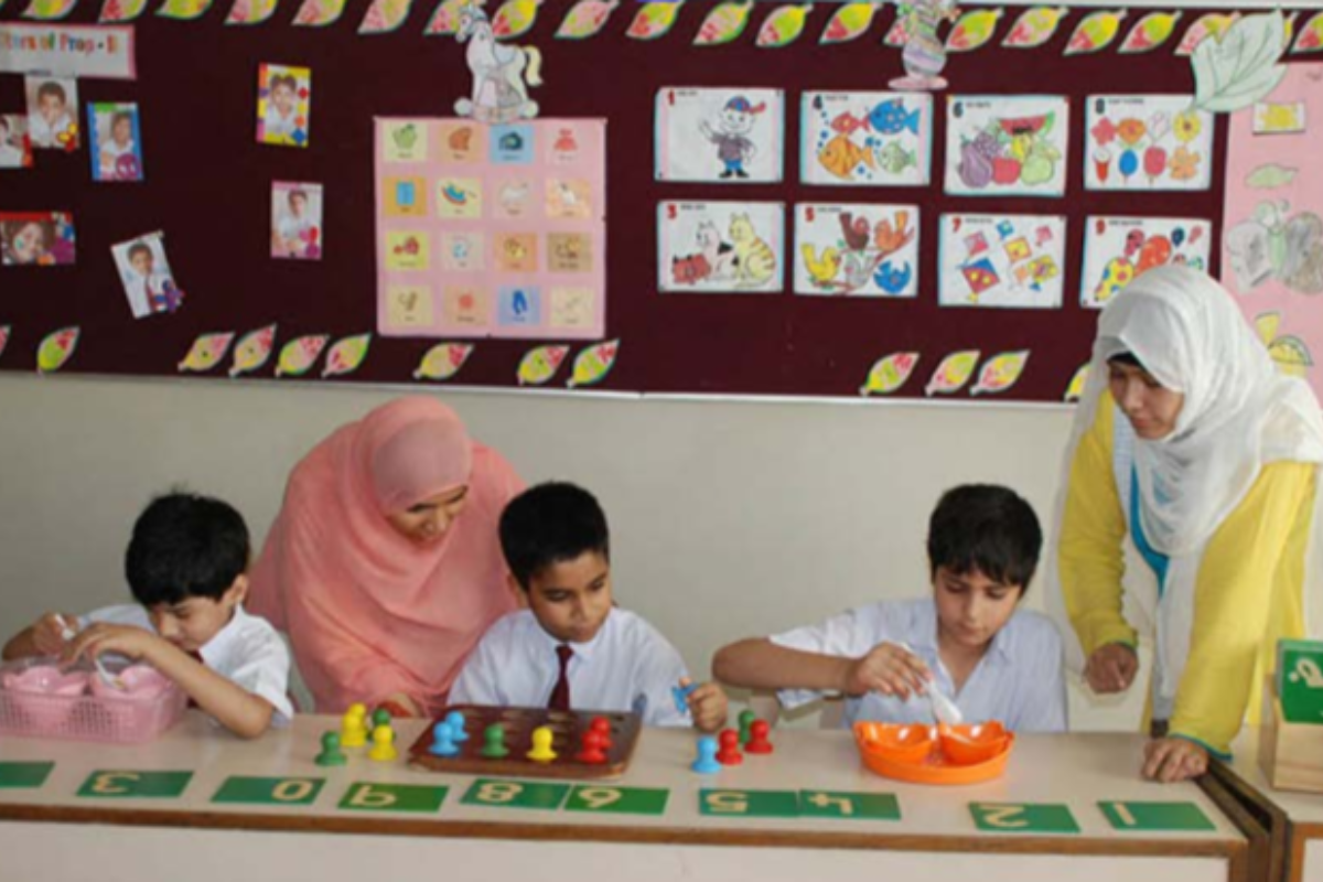 Two teachers helping three boys with their schoolwork in a classroom.