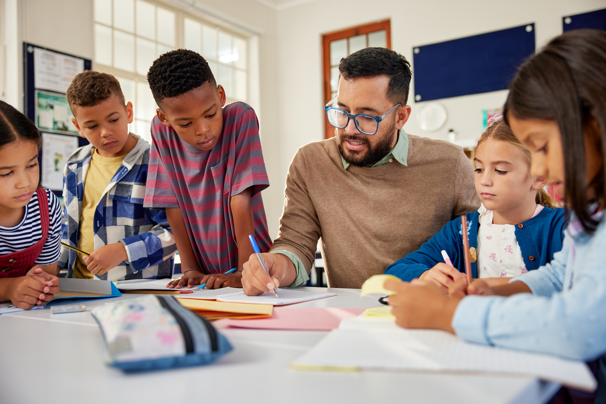 Teacher seated at a table speaking to young students