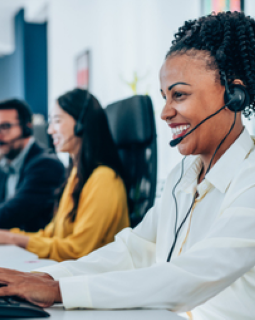 Woman at a call center wearing a headset. Others in background.