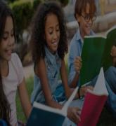 Young school children with backpacks and notebooks sitting outdoors in the grass