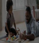 Young father and young son play with wooden block toys on living room floor