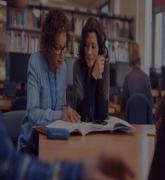 Teacher with mature female adult student sitting at table working in college library