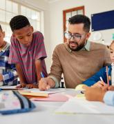 Teacher seated at a table speaking to young students
